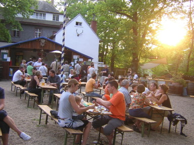 Gäste beim Essen an Biertischen im abendlichen Waldbiergarten